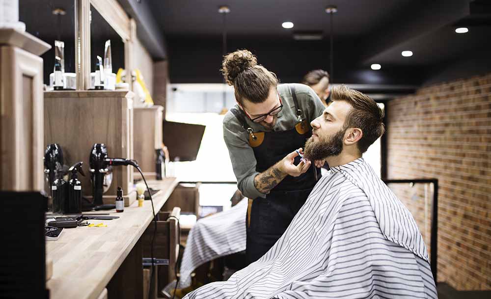 Barbero atendiendo y afeitando a un cliente en su local