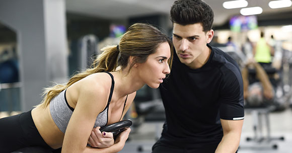 Entrenador personal con un cliente en un gimnasio realizando ejercicios.